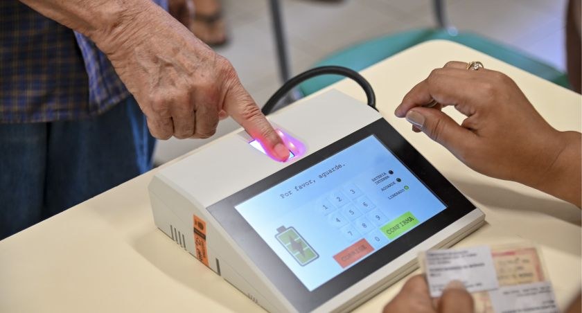 Homem posiciona o dedo indicador da mão direita em um leitor biométrico no terminal do mesário.