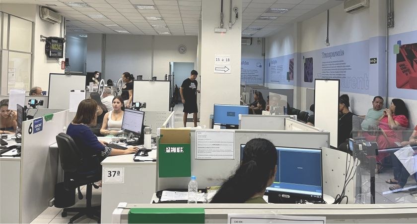Foto mostra uma Central de Atendimento ao Eleitor, com eleitores e servidores junto a guichês de...