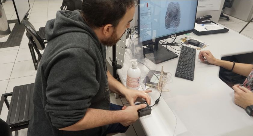 Foto mostra um homem branco de barba com o dedo indicador direito sobre um leitor biométrico. A ...