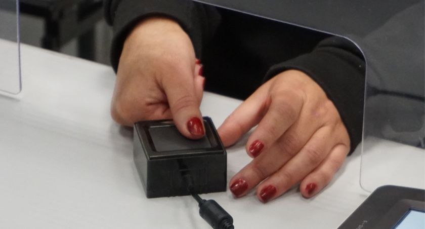 Foto de uma mão feminina com esmalte vermelho nas unhas fazendo a coleta das digitais em um equi...