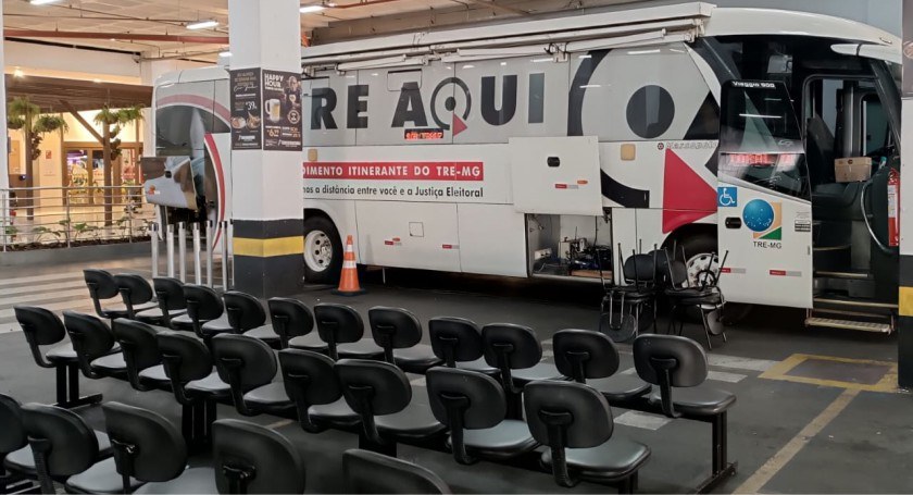 Foto mostra um ônibus branco com plotagem TRE Aqui na lateral. O veículo está em um estacionamen...