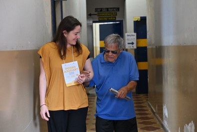 Coordenadora de acessibilidade auxilia um eleitor com deficiência visual