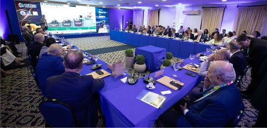 Foto mostra presidentes dos TREs sentados ao redor de uma mesa em formato de U. Ao fundo, um hom...