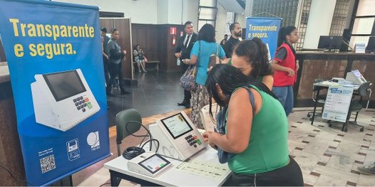 Eleitora é filmada por jornalista enquanto treina o voto na urna eletrônica com simulador.