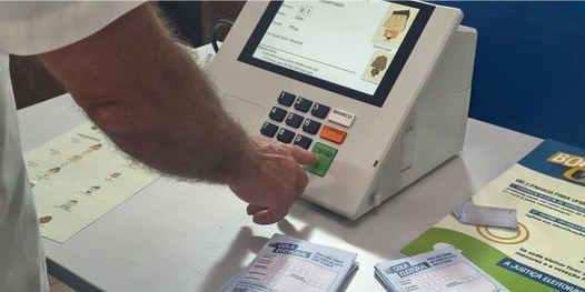 Eleitora é filmada por jornalista enquanto treina o voto na urna eletrônica com simulador.