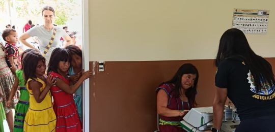 Diversos indígenas observam cartazes colados na parede de uma escola.