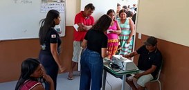 Um homem indígena vota na urna eletrônica. Ele é observado por duas servidoras do TRE-MG e algun...