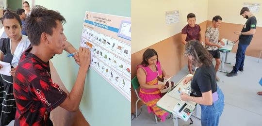 Diversos indígenas observam cartazes colados na parede de uma escola.