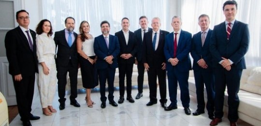 Fota mostra homens e mulheres sentados ao redor de uma grande mesa em formato de U.