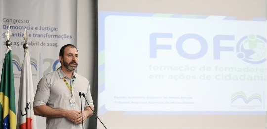Foto do servidor do TRE-MG Marcelo Bortolo. Atrás dele, aparecem as bandeiras do Brasil e de Min...