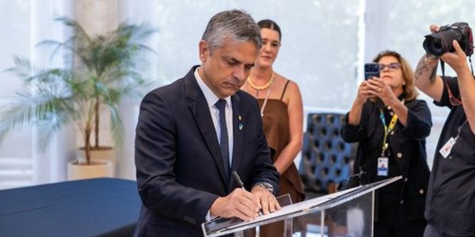 Presidente do TRE-MG assina documento. Ao fundo, pessoas fotografando o momento.