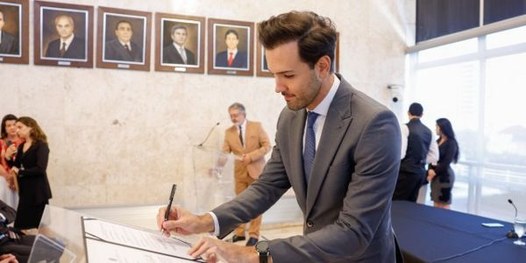 Presidente do TRE-MG assina documento. Ao fundo, pessoas fotografando o momento.