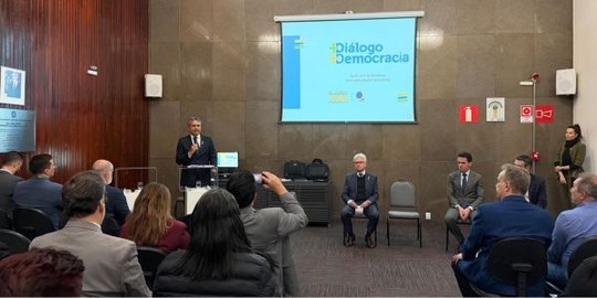 Foto mostra o desembargador Carlos Henrique Perpétuo Braga de pé, no canto esquerdo. Em primeiro...