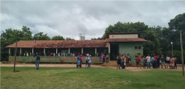 Foto de escola indígena na Aldeia Tenda. Várias pessoas estão em fila na varanda da escola.