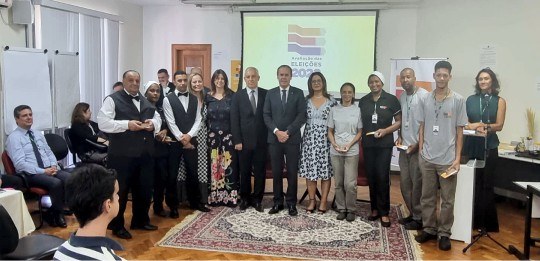 Vários homens e mulheres, de pé, posam para a foto. Atrás deles, um telão com a logomarca Avalia...