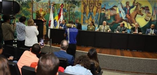 Foto da cacica Ãgohó durante discurso. Ela está de pé no canto esquerdo, vestindo saia de palha ...