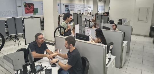 Foto mostra eleitores e servidores em guichês de atendimento na Central de Atendimento ao Eleito...