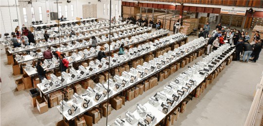 Carga das urnas BH 2022 Dezenas de urnas eletrônicas sobre bancadas em um galpão