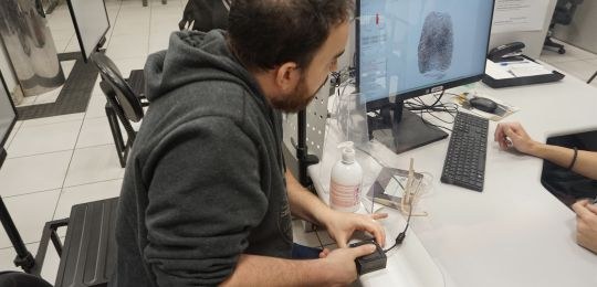 Foto mostra um homem branco com o dedo indicador sobre um leitor biométrico. A imagem da digital...