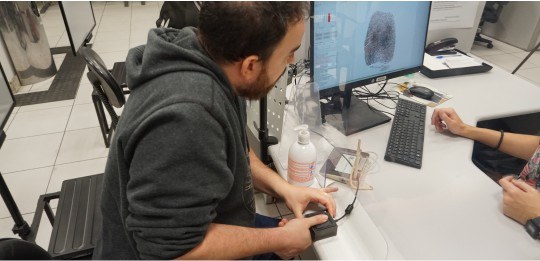 Homem com dedo posicionado no leitor biométrico e digital aparecendo na tela do computador.
