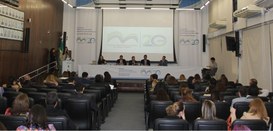 Foto mostra a plateia de um auditório em primeiro plano e cinco homens sentados junto a uma mesa...