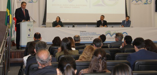 Foto mostra parte da plateia em primeiro plano. Ao fundo, ministro Afrânio Vilela de pé junto a ...