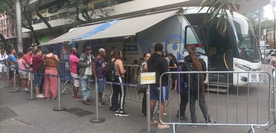 Foto mostra uma fila de pessoas junto ao ônibus com identidade visual TRE Aqui