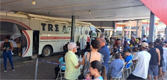 Foto mostra uma fila de pessoas junto ao ônibus com identidade visual TRE Aqui