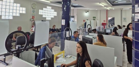 Foto mostra uma fila de pessoas junto ao ônibus com identidade visual TRE Aqui