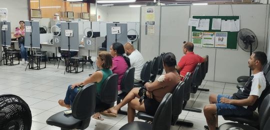 Foto mostra uma fila de pessoas junto ao ônibus com identidade visual TRE Aqui