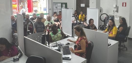 Foto mostra uma fila de pessoas junto ao ônibus com identidade visual TRE Aqui