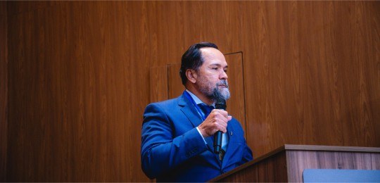 Desembargador Ramom Tácio segura um microfone com a mão direita, durante discurso.