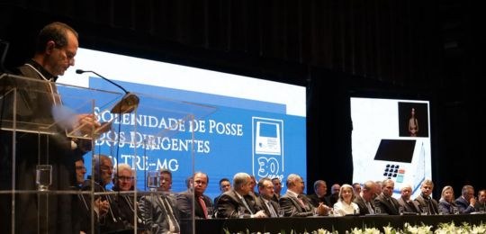Foto mostra um teatro lotado. Ao fundo, diversas pessoas sentadas junto a uma mesa sobre o palco.