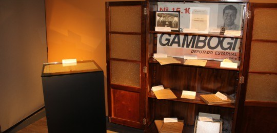 Doações para o Centro de Memória Documentos em exposição em uma estante de madeira.