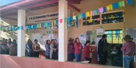 Foto mostra eleitores no corredor de uma escola, que está decorado com bandeirinhas coloridas.
