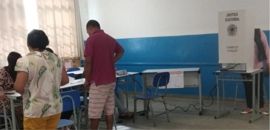 Foto mostra eleitores e mesários dentro de uma seção eleitoral.