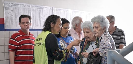 Foto mostra duas idosas conversando com uma representante da Justiça Eleitoral