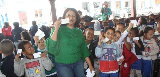 A teacher and several children hold voting cards