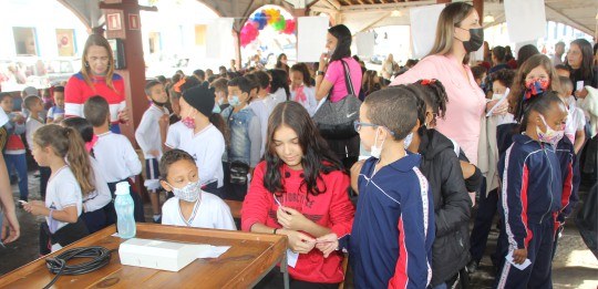 In the front row, a boy gives a document to a girl.  Several children in the background.