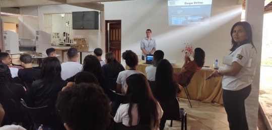 Jovens sentados acompanham a palestra de um homem.