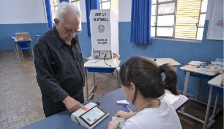 Foto mostra eleitor idoso fazendo a identificação biométrica em uma seção eleitoral.