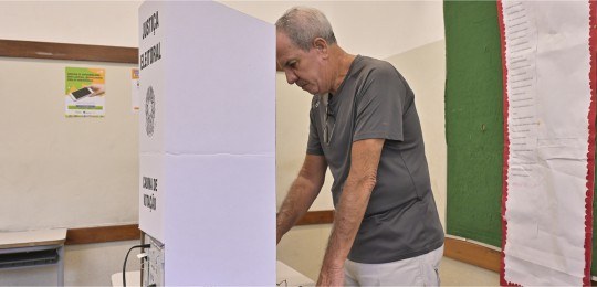 Foto mostra um homem de cabelos grisalhos na cabine de votação. Belo Horizonte/MG/2024