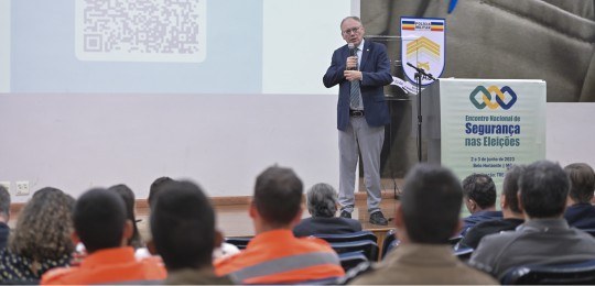 Encerramento Encontro Nacional de Segurança nas Eleições Desembargador Paulo Tamburini de pé no palco. Em primeiro plano, parte da plateia.