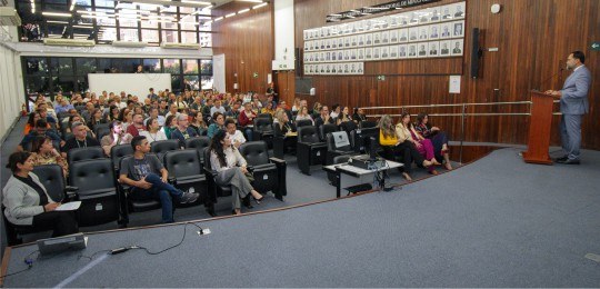 No canto direito, o desembargador Ramom Tácio está de pé em um palco. No restante da foto, apare...