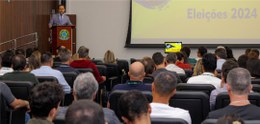 Em primeiro plano, parte de um auditório, com as pessoas de costas. Ao fundo, o desembargador Ra...