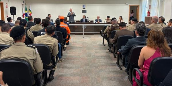 Foto do Salão do Júri em Uberlândia. Ao fundo, autoridades sentadas junto a uma mesa e o desemba...