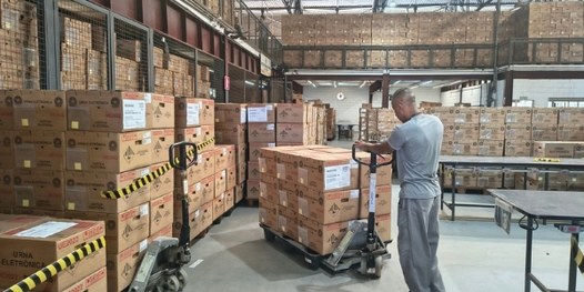 Pilhas de caixas de urnas eletrônicas dentro de um galpão