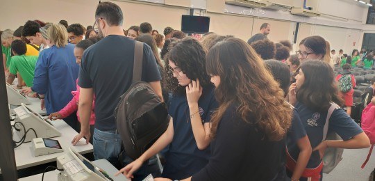 Foto mostra um auditório lotado de estudantes. No canto direito, o servidor do TRE Paulo Trindad...