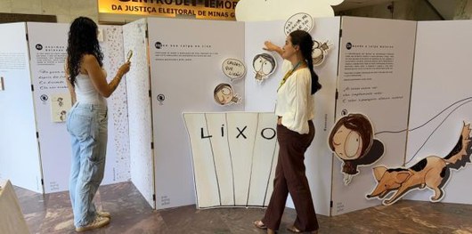 Foto mostra duas mulheres interagindo com elementos nos painéis de uma exposição.