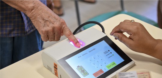 Foto em close de eleitor posicionando o dedo no leitor biométrico.